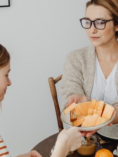 Mother and daughter enjoying a healthy breakfast together with fresh fruits and juice.