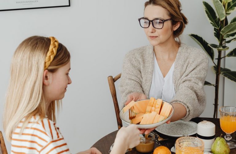 Mother and daughter enjoying a healthy breakfast together with fresh fruits and juice.