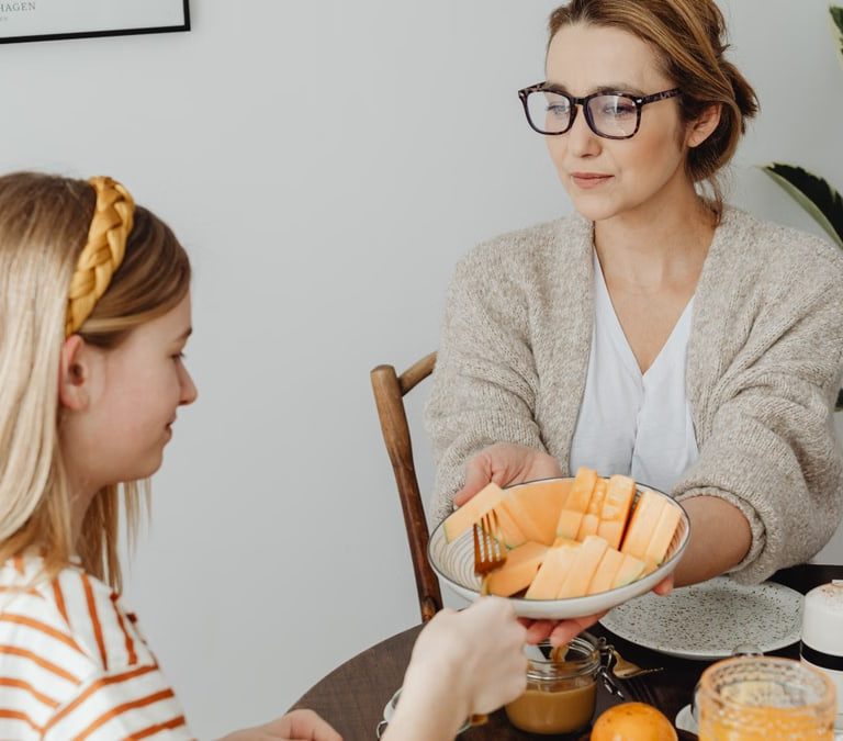 Mother and daughter enjoying a healthy breakfast together with fresh fruits and juice.