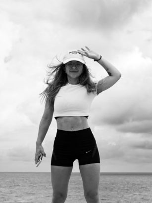 Woman in sportswear stands confidently by the sea against a cloudy sky.