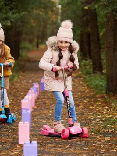 Two girls having fun on scooters in a leafy autumn park trail.